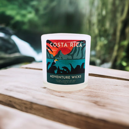 Costa Rica Travel-Inspired Soy Candle sitting on wooden table with green foliage in background